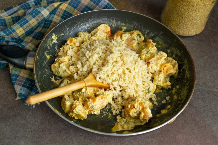 Combining pumpkin with the creamy sauce and cooked bulgur Adding cooked bulgur to the skillet with pumpkin simmering in a creamy sauce.