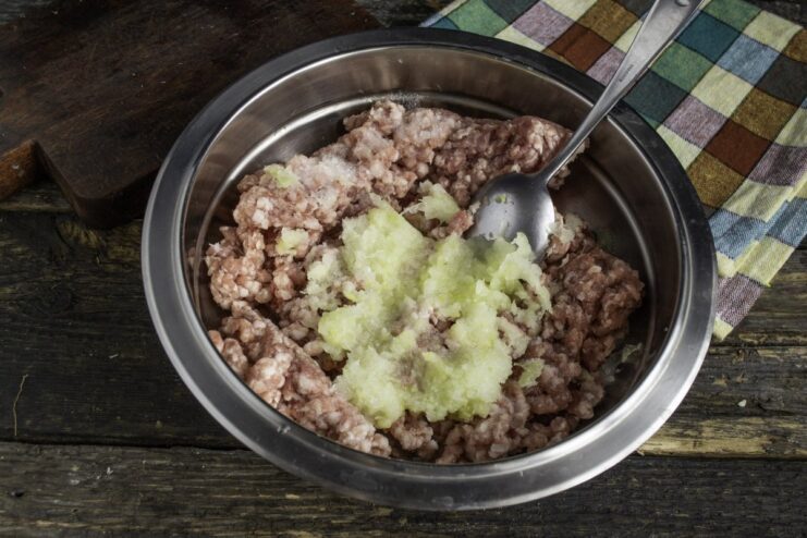 Preparing the Meat Patty Mixture with Grated Onion A bowl of ground meat with freshly grated onion being added.