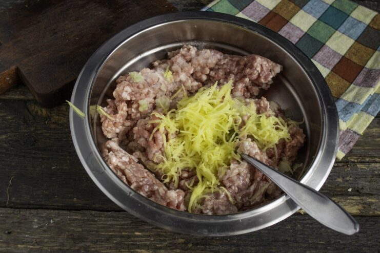 Adding Grated Potato for Extra Juiciness Grated raw potato being added to the ground meat mixture in a bowl.