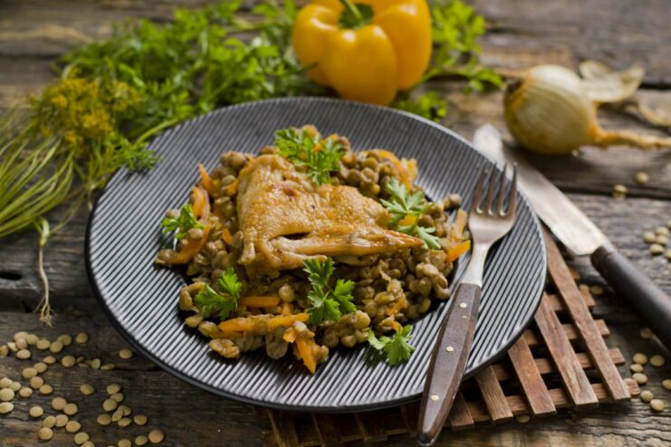 A plate of cooked lentils with chicken and vegetables, garnished with fresh herbs.