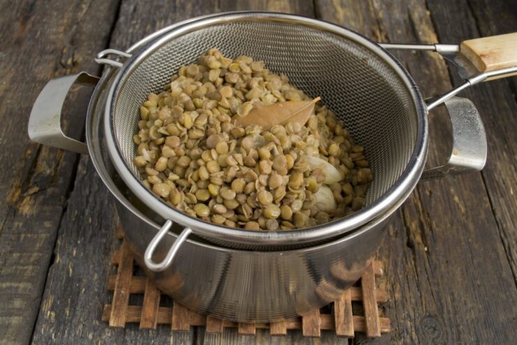 Draining the Cooked Lentils in a Colander to Remove Excess Water Cooked green lentils being drained in a white colander in a kitchen sink.