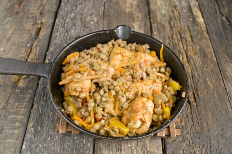 Adding the Golden-Brown Chicken Wings to the Lentil and Vegetable Stew Placing pan-fried chicken wings on top of the lentil and vegetable mixture in a skillet.