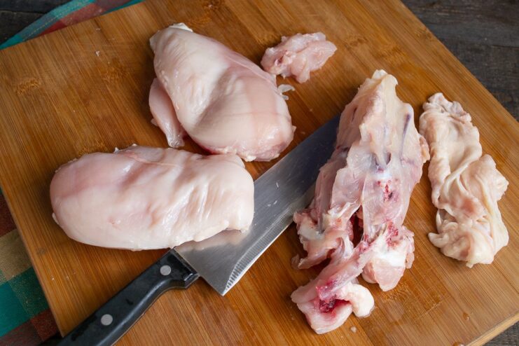 Preparing Chicken Fillet for the Roll Casing Raw chicken breast on a cutting board, being sliced and diced for the meat roll.