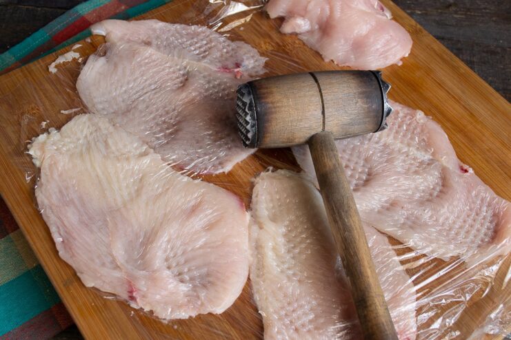 Pounding the Chicken Fillet Thin A thin slice of chicken fillet being pounded with a meat mallet.
