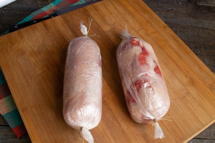 Securing the Roll for Cooking A meat roll tightly wrapped in multiple layers of plastic wrap and tied with kitchen twine.