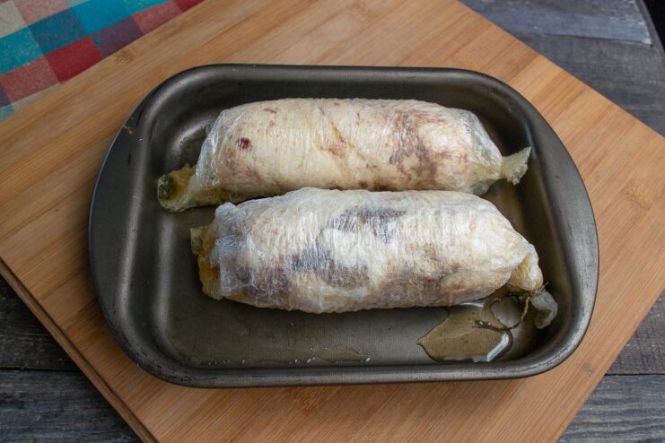 Slow-Cooking the Meat Rolls Two wrapped meat rolls simmering gently in a pot of hot water on the stove.