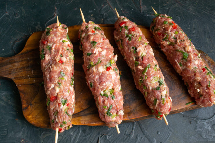 How to Shape Casing-Free Sausages on Skewers A hand shaping a ground meat mixture around a bamboo skewer to form a sausage.