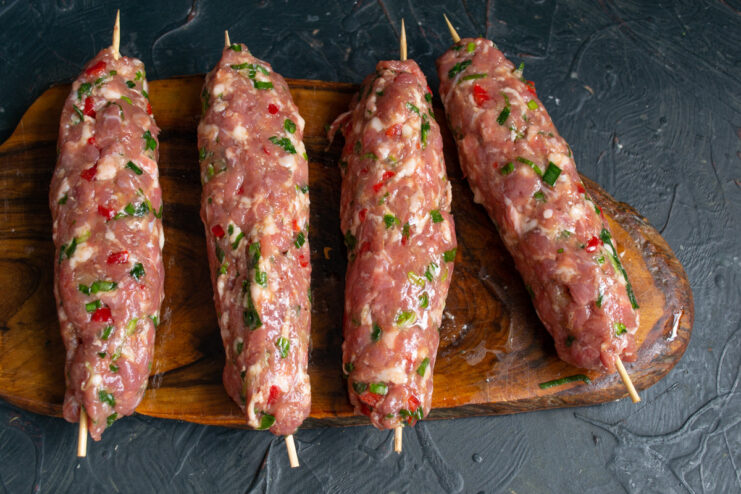 Greasing the Sausages with Oil Before Cooking A hand rubbing vegetable oil onto a raw sausage on a skewer before frying.