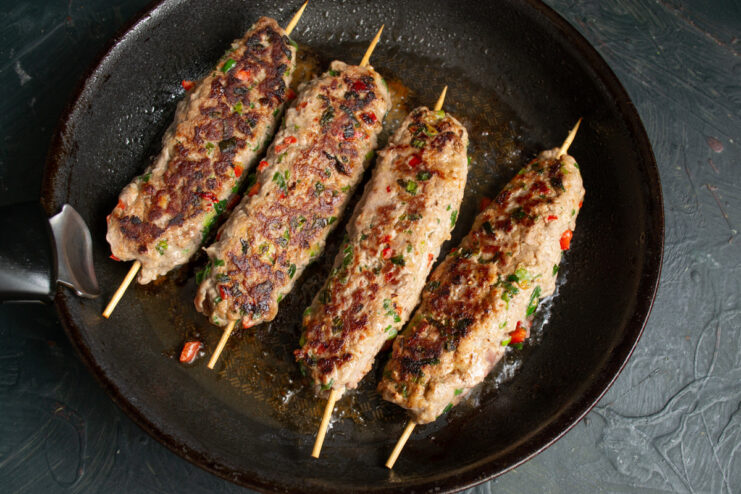 Pan-Frying Homemade Sausages Until Golden Brown Four homemade sausages on skewers sizzling in a hot grill pan.