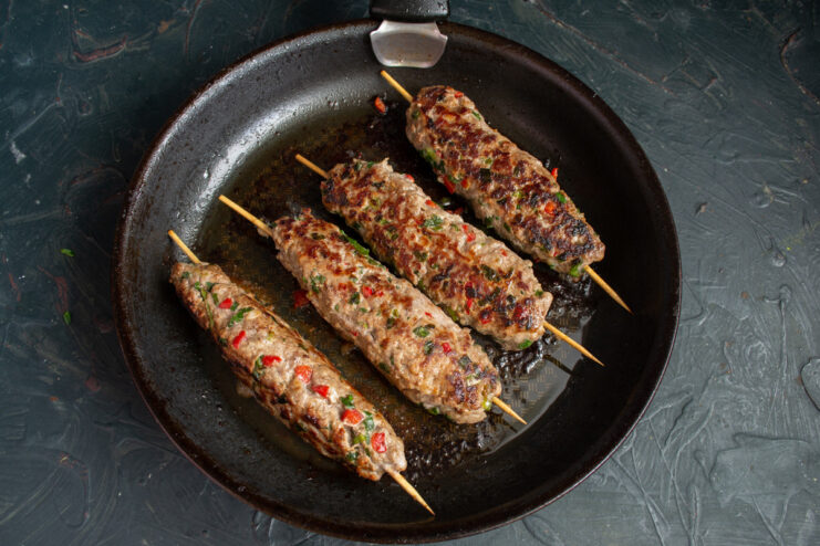 Serving Homemade Sausages with Your Favorite Sauce Cooked homemade sausages on skewers served on a plate with a side of ketchup.