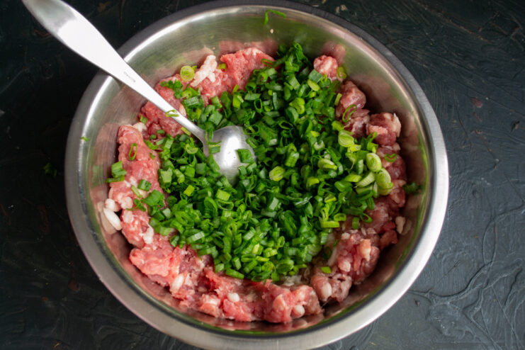 Adding Fresh Green Onions to the Sausage Mixture A hand adding finely chopped green onions to a bowl of ground meat.