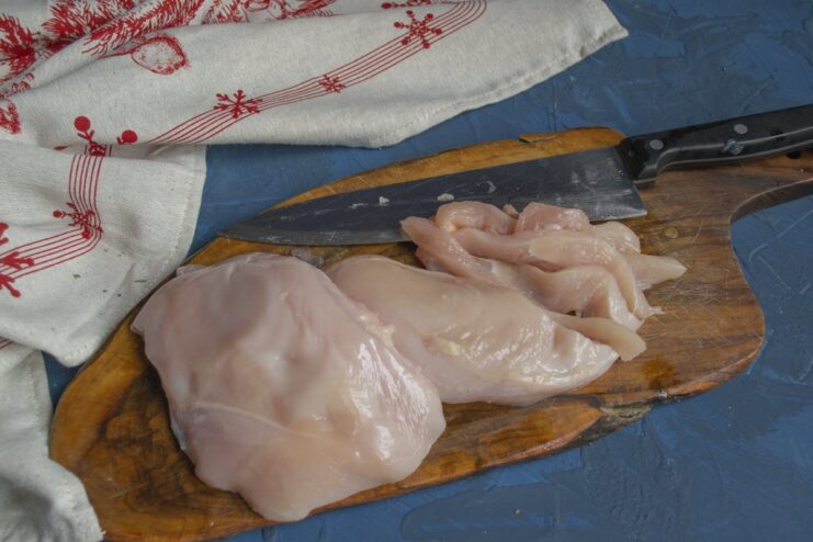 Slicing Chicken Fillet for Grinding Raw chicken breast fillet being sliced into thin strips on a cutting board.
