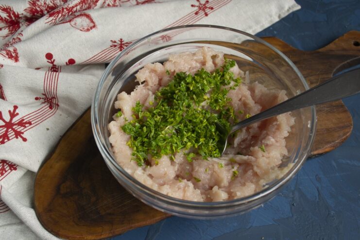 Adding Fresh Herbs to the Filling Finely chopped fresh parsley being added to the bowl of ground chicken.