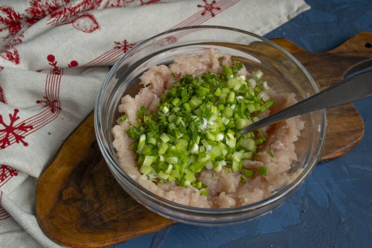 Flavoring the Meat with Green Onions Finely chopped green onions are added to the ground meat mixture in a bowl.