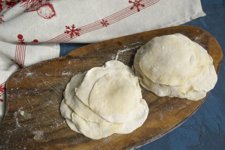 Rolling Out Thin Circles for Pelmeni Small pieces of dough being rolled out into thin, round wrappers for pelmeni.