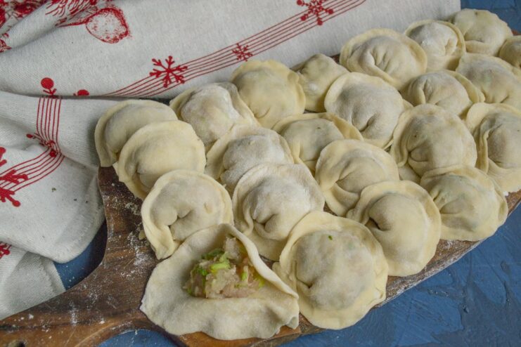 Shaping the Homemade Pelmeni Hand-shaped raw pelmeni dumplings arranged on a floured wooden board.