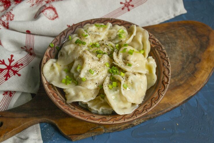 Serving Pelmeni with Butter and Herbs A bowl of hot, cooked pelmeni drizzled with melted butter and garnished.
