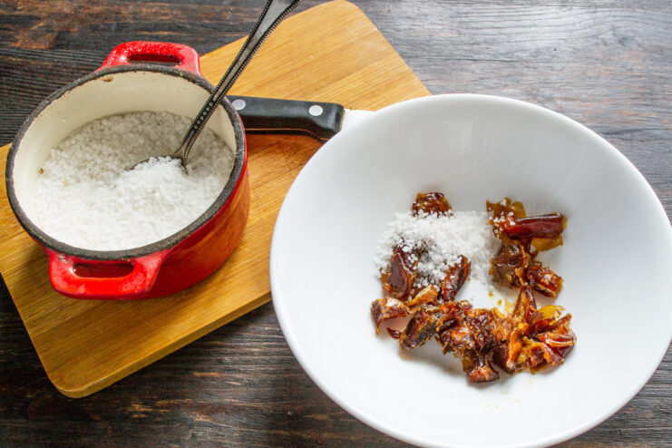 Seasoning the Dates with Sea Salt Adding a spoonful of sea salt to a bowl of chopped dates.
