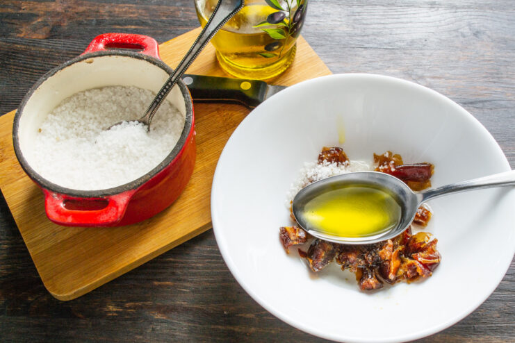 Adding Extra Virgin Olive Oil for Richness Pouring extra virgin olive oil into the bowl with dates and salt.