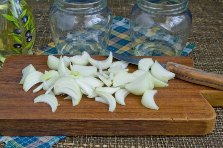 Step 1: Layering the Onions for the Chicken and Potato Preserve Close-up of glass jars with a layer of chopped onions at the bottom.