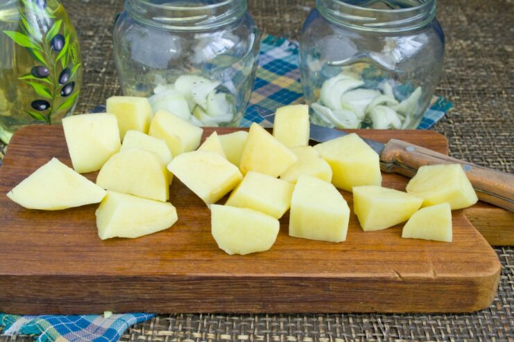Building the Layers: Adding Potatoes to the Jars Glass jars being filled with a layer of diced potatoes over the onions.
