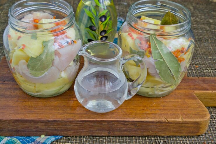 Adding Liquid: Pouring Water into the Jars Before Baking Pouring a small amount of warm water into the jars filled with chicken, potatoes, and spices.