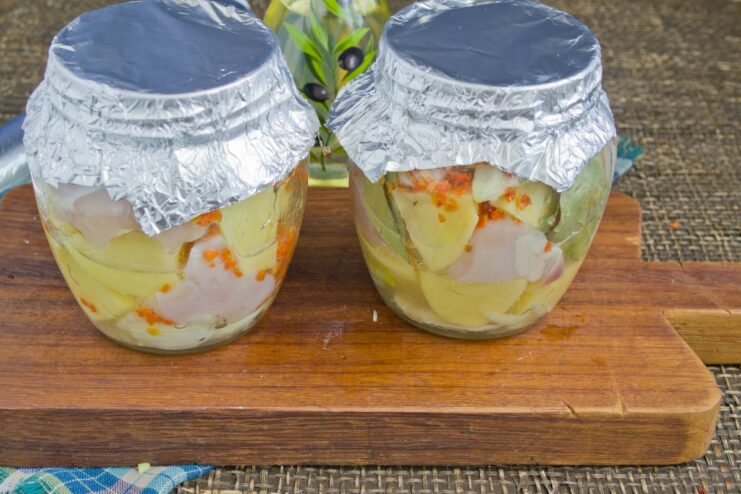 Preparing for the Oven: Covering Jars with Aluminum Foil Glass jars filled with ingredients, with their openings covered tightly with aluminum foil.