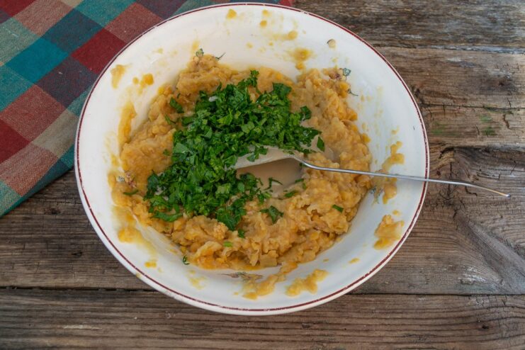 A handful of chopped fresh parsley being added to the chickpea mixture in a bowl.