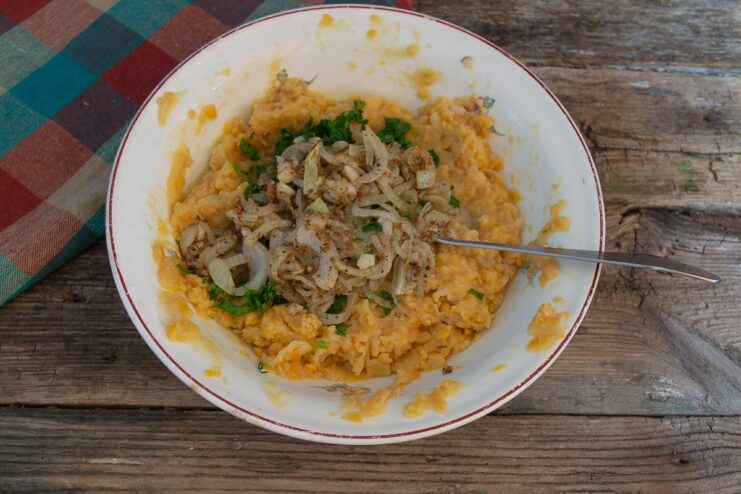 Sautéed onions, garlic, and spices are added to the bowl of mashed chickpeas.