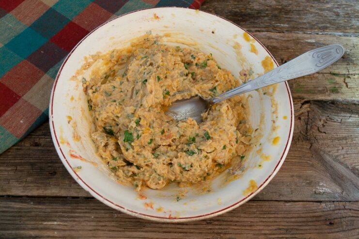 A person's hands thoroughly mixing the falafel dough in a glass bowl.