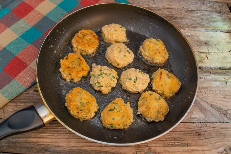 Small, round falafel balls being carefully placed into a pan with hot oil for frying.