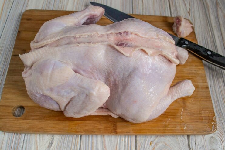 Step 1: Carefully make an incision down the chicken's back A raw chicken lying breast-down with a knife cutting the skin along its spine.