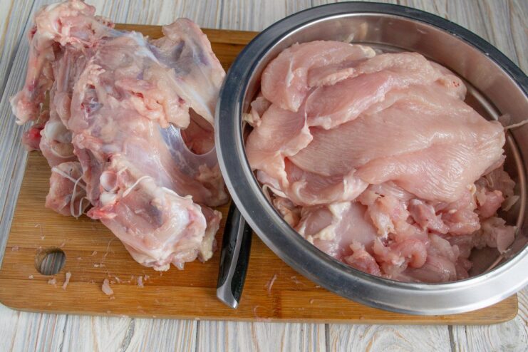 Deboning the chicken: separating all the meat from the carcass Hands using a knife to cut chicken meat away from the bones.