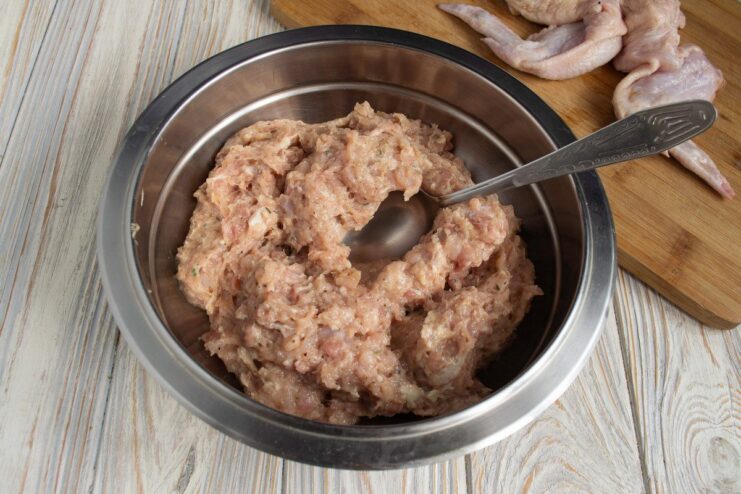 Using a meat grinder to prepare the chicken filling A meat grinder processing chicken meat into a bowl of mince.