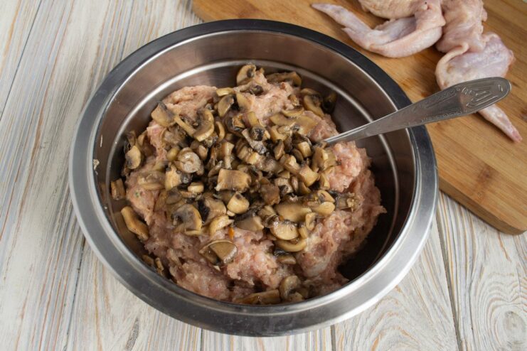 Adding sautéed mushrooms to the chicken mince for a rich filling A bowl of raw chicken mince with sautéed mushrooms being added.