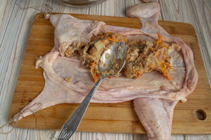 Carefully stuffing the chicken skin with the prepared filling Hands stuffing the chicken skin with the meat and vegetable mixture.