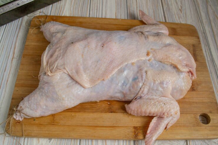 Shaping and securing the stuffed chicken before baking A stuffed raw chicken being sewn shut with kitchen twine.