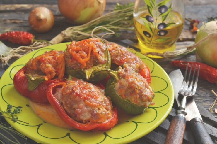 A plate of baked stuffed peppers with minced meat, served with sour cream and fresh herbs.
