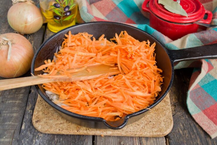 Adding Grated Carrots to the Sautéed Onions Grated carrots being added to the pan with sautéed onions.