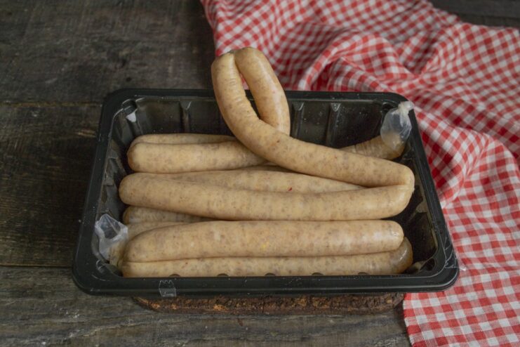 Preparing Sausages: Tying the Casings to Keep Them Juicy Close-up of hands tying the ends of raw sausage casings with kitchen twine.