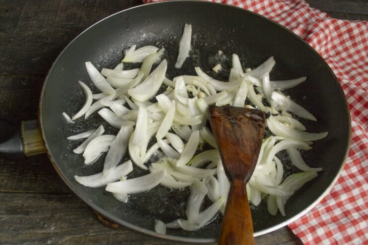Building Flavor: Sautéing Onions and Garlic in a Pan Sliced onions and garlic being sautéed in a skillet until translucent.