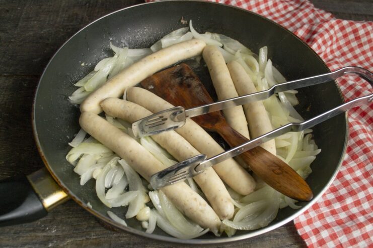 Frying Sausages with Onions Until Golden Brown Parboiled sausages being fried in a skillet with onions.