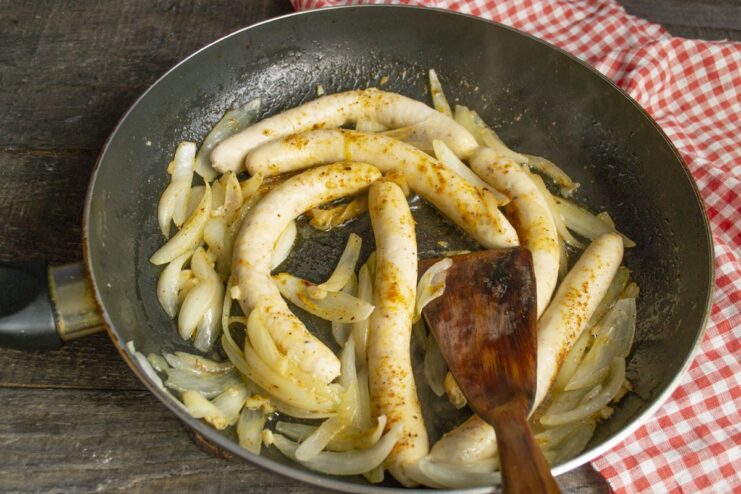 Seasoning the Dish with Aromatic French Herbs Sprinkling dried French poultry seasoning over sausages and onions in a skillet.