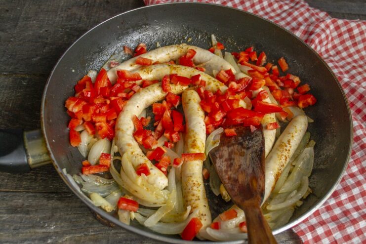Adding Fresh Vegetables: Cooking Bell Peppers with Sausages Chopped red bell pepper being added to the skillet with sausages and onions.