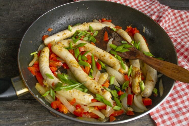 Finishing Touch: Adding Fresh Green Onions Chopped green onions being sprinkled over the cooked sausages and vegetables in the pan.