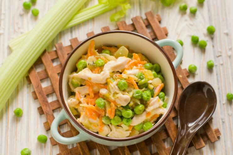 A white bowl filled with creamy chicken fricassee with green peas, served as a French-style stew.