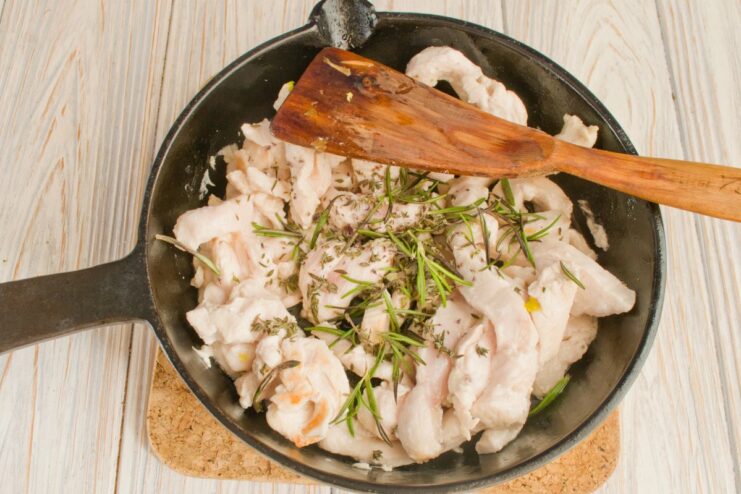 Searing Chicken Strips Until Lightly Golden Thin strips of chicken being pan-fried in a skillet with herbs.