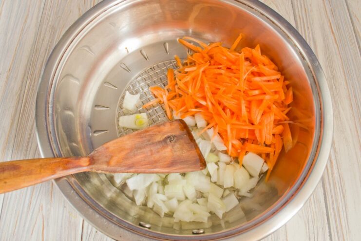 Adding Julienned Carrots to the Sautéed Onions Julienned carrots being added to the skillet with sautéing onions.