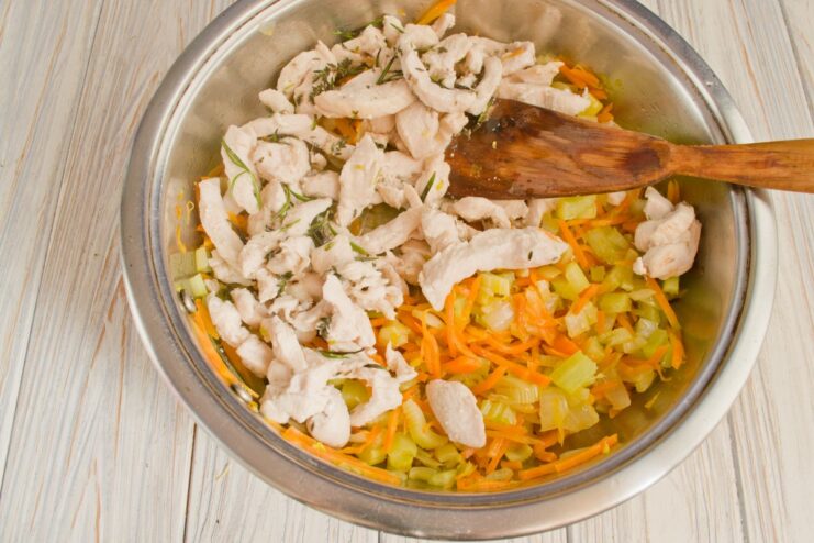 Combining Seared Chicken with Sautéed Vegetables Cooked chicken strips being added to the skillet with the sautéed vegetable mix.