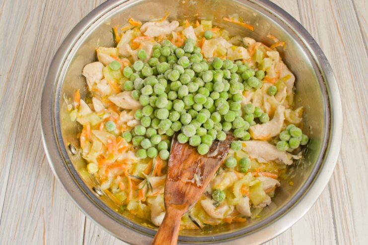 Finishing the Fricassee with Green Peas Frozen green peas being added to the creamy chicken fricassee in the skillet.